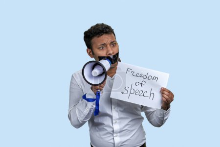 Téléchargez les photos : Jeune homme indien avec mégaphone et liberté d'expression iscription. Isolé sur fond bleu pâle. - en image libre de droit