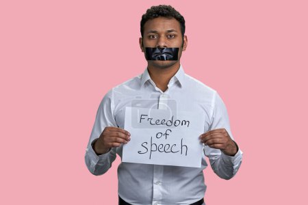 Téléchargez les photos : Homme indien avec la bouche enregistrée et l'inscription de la liberté d'expression. Isolé sur fond rose. - en image libre de droit