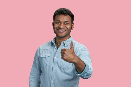 Foto de Joven sonriente hombre del sur de Asia mostrando un pulgar hacia arriba. Feliz chico exitoso dando lo suyo. Aislado sobre fondo rosa. - Imagen libre de derechos