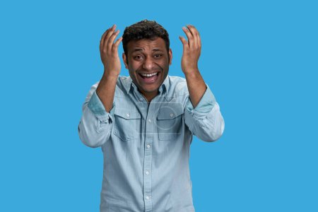 Photo for Young arab man is looking at something ridiculous and laughing. Isolated on blue. - Royalty Free Image