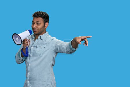 Photo for Young brown indian man speaking in megaphone and pointing at something. Isolated on vivid blue background. - Royalty Free Image