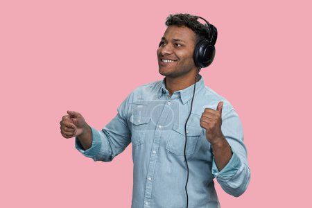 Téléchargez les photos : Souriant homme indien joyeux appréciant la musique dans les écouteurs. Isolé sur fond rose. - en image libre de droit