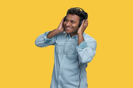 Téléchargez les photos : Portrait d'homme indien marron heureux appréciant la musique dans les écouteurs. Isolé sur fond jaune vif. - en image libre de droit