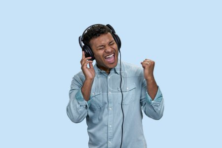 Photo for Portrait of excited emotional Indian man listen to music in headphones. Isolated on pastel blue background. - Royalty Free Image