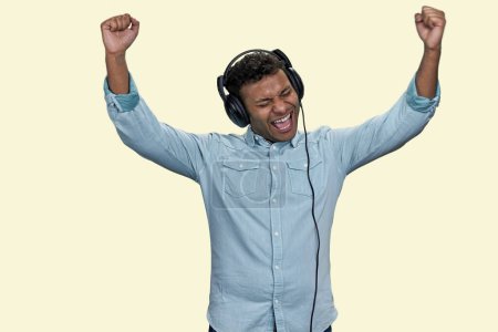 Foto de El joven indio emocional usa una camisa azul para escuchar música en los auriculares. Aislado sobre fondo blanco. - Imagen libre de derechos