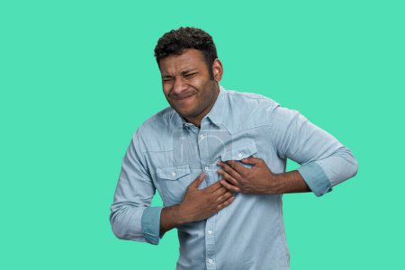Photo for Young indian man having a pain in the heart. Brown guy with heart attack. Isolated on green background. - Royalty Free Image