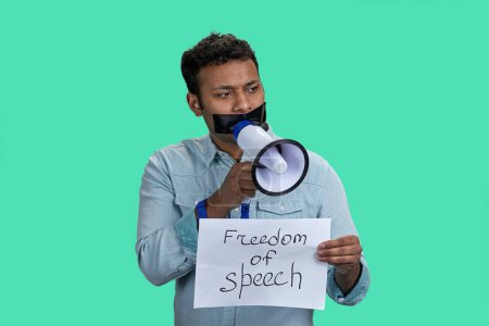 Photo for Portrait of indian man with taped mouth is holding megaphone. Sheet of paper with freedom of speech inscription. Isolated on green background. - Royalty Free Image