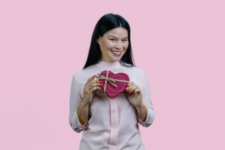 Photo for Happy cheerful young asian woman with heart shape gift box. Isolated on pink background. - Royalty Free Image