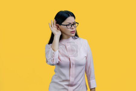 Téléchargez les photos : Portrait d'une jeune femme asiatique entendant des commérages. Isolé sur fond jaune. - en image libre de droit