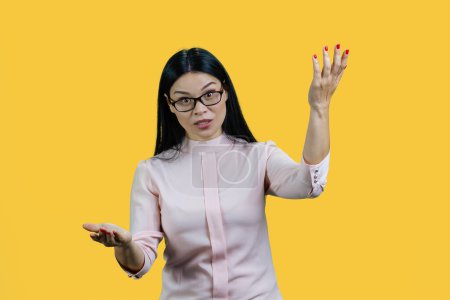 Foto de Desagradable joven asiática empresaria está explicando algo. Aislado sobre fondo amarillo. - Imagen libre de derechos