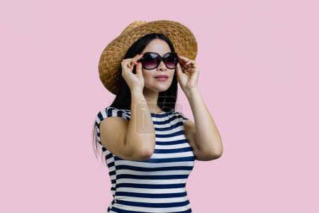 Téléchargez les photos : Jeune touriste asiatique femme porte un chapeau de paille et des lunettes de soleil. Isolé sur fond rose. - en image libre de droit