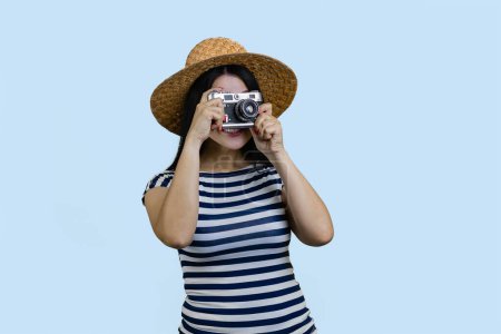 Photo for Young brunette female tourist taking a photo on vintage photo camera. Isolated on blue. - Royalty Free Image