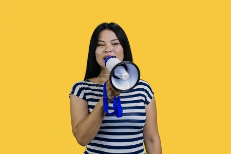 Photo for Young asian woman saying something in a megaphone. Isolated on yellow. - Royalty Free Image
