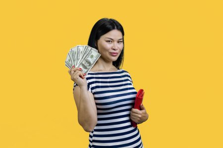 Photo for Asian woman is showing fan of dollar banknotes. Standing over yellow background. - Royalty Free Image