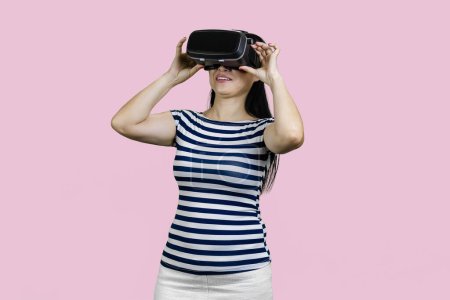 Photo for Happy young black lady in VR glasses exploring cyberspace. Playing virtual reality game. Isolated on pink. - Royalty Free Image