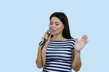 Photo for Young asian woman is singing a song in microphone. Isolated on pale blue background. - Royalty Free Image