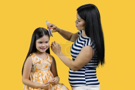 Téléchargez les photos : Jeune mère asiatique peigne sa fille. Isolé sur jaune. - en image libre de droit