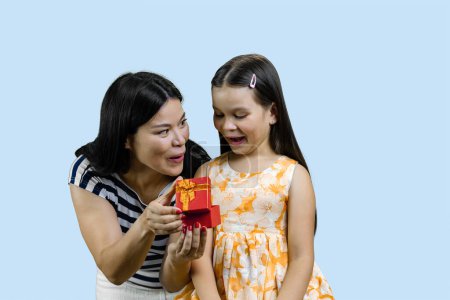Téléchargez les photos : Jeune femme brune donne une boîte cadeau ouverte à sa petite princesse heureuse. Isolé sur fond bleu pâle. - en image libre de droit