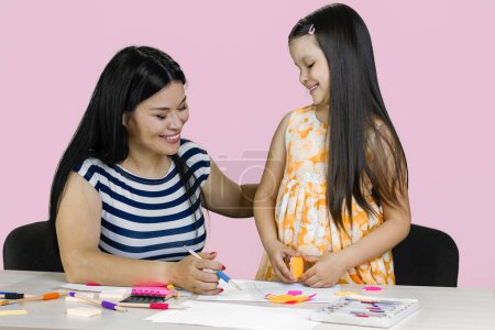 Foto de Madre y su hija están dibujando y haciendo recortes de papel. Aislado en rosa. - Imagen libre de derechos