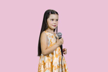 Foto de Linda niña en vestido está sosteniendo un micrófono. Aislado en rosa. - Imagen libre de derechos