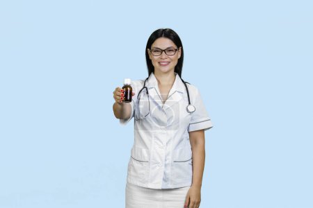 Téléchargez les photos : Portrait d'une jeune femme asiatique médecin donne bouteille de médicament. Isolé sur fond bleu. - en image libre de droit