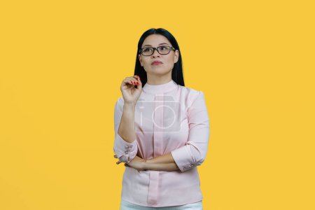 Téléchargez les photos : Portrait d'une jeune femme d'affaires asiatique réfléchie. Isolé sur jaune. - en image libre de droit