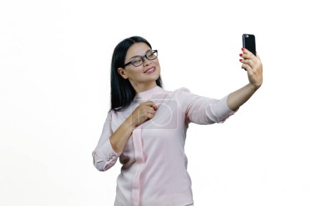 Foto de Atractiva joven asiática mujer en gafas está tomando una selfie en la cámara frontal. Aislado sobre fondo blanco. - Imagen libre de derechos
