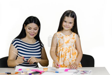 Téléchargez les photos : Mère et fille à table avec des crayons et des papiers colorés. Dessiner et faire des découpes de papier. Isolé sur blanc. - en image libre de droit
