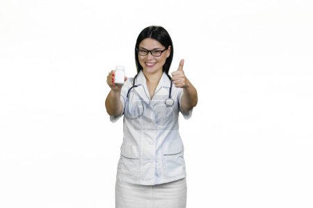 Téléchargez les photos : Médecin souriante avec une bouteille blanche de pilules donnant un pouce vers le haut. Isolé sur blanc. - en image libre de droit