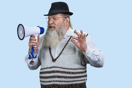 Téléchargez les photos : Portrait d'un homme barbu âgé prononçant un discours en mégaphone. Isolé sur fond bleu pastel. - en image libre de droit