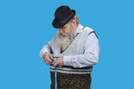 Photo for Senior man measuring waist with a blue tape. Lose weight concept. Isolated on vivid blue background. - Royalty Free Image