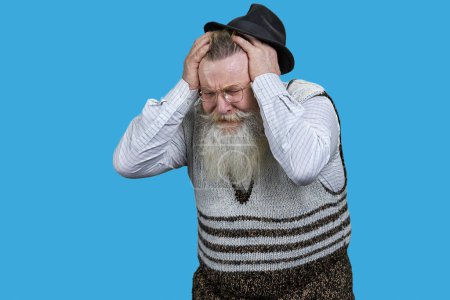 Téléchargez les photos : Vieil homme retraité avec une longue barbe qui a terriblement mal à la tête. Fond bleu vif. - en image libre de droit