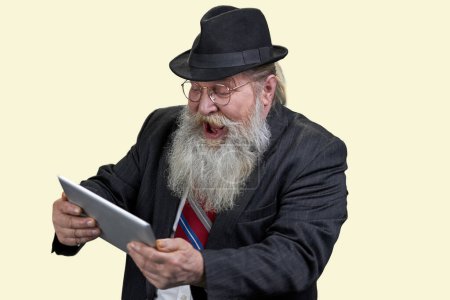 Téléchargez les photos : Portrait de l'homme âgé excité avec tablette pc. Isolé sur jaune. - en image libre de droit