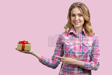 Photo for Attractive young blond woman is pointing at gift box. Isolated on pink background. - Royalty Free Image