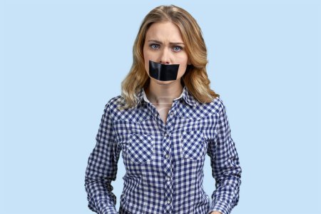 Photo for Portrait of angry stressed blond woman with mouth taped. Pastel blue background. - Royalty Free Image