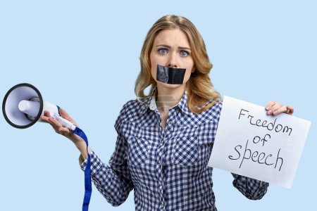 Téléchargez les photos : Jeune femme blonde avec la bouche scotchée tenant mégaphone et bannière. Concept de liberté d'expression. - en image libre de droit