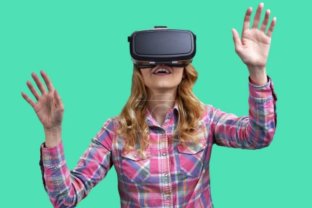 Photo for Portrait of a expressive young woman enjoying vr experience with her hands up. Isolated on green background. - Royalty Free Image