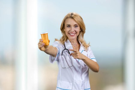 Téléchargez les photos : Heureux médecin blonde bouteille de médecine publicitaire. Pointant sur les pilules. - en image libre de droit