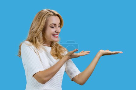 Téléchargez les photos : Femme caucasienne mature présentant l'espace de copie avec les deux mains. Isolé sur bleu. - en image libre de droit