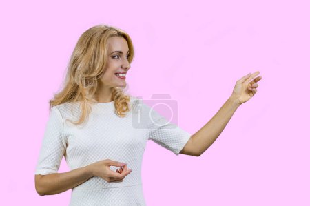 Téléchargez les photos : Heureuse femme blonde mature pointant vers l'espace de copie. Isolé sur rose. - en image libre de droit