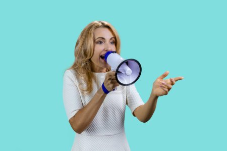 Photo for Attractive expressive blonde woman screaming in megaphone. Isolated on turquoise. - Royalty Free Image