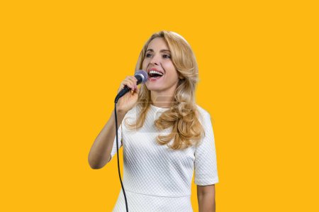 Photo for Pretty mature blond woman singing in microphone. Isolated on vivid yellow. - Royalty Free Image