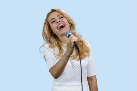 Téléchargez les photos : Portrait de femme blonde mature heureuse chantant au microphone. Isolé sur bleu pâle. - en image libre de droit