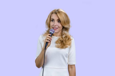 Téléchargez les photos : Portrait d'une jolie femme blonde mature tenant un microphone et donnant un discours. Isolé sur violet. - en image libre de droit