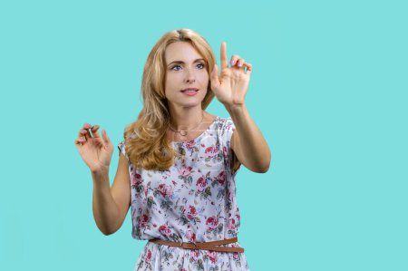 Téléchargez les photos : Portrait de femme blonde cliquez sur un bouton sur un écran virtuel imaginaire invisible. Isolé sur turquoise. - en image libre de droit