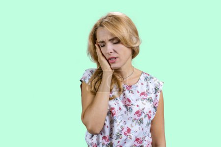 Photo for Portrait of mature blonde woman touching her cheek because of toothache. Dental illness on teeth. Isolated on turquoise. - Royalty Free Image