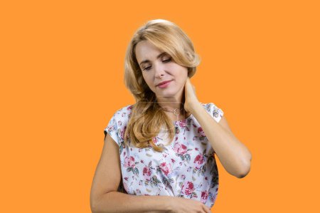 Téléchargez les photos : Portrait de femme blonde mature souffre de maux de cou. Isolé sur orange. - en image libre de droit