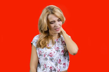 Photo for Portrait of middle middleaged caucasian blonde woman having a neck pain. Isolated on red. - Royalty Free Image