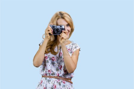 Foto de Retrato de mujer rubia caucásica tomando una foto usando una cámara de fotos retro vintage. Aislado en azul pastel. - Imagen libre de derechos