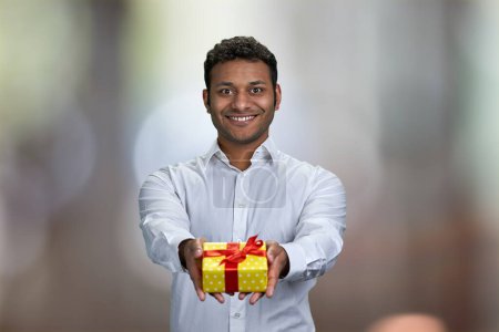 Jeune homme d'affaires beau offrant boîte cadeau sur fond bokeh abstrait. Concept de célébration d'anniversaire.
